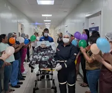 Paciente é aplaudida por profissionais de saúde em corredor de hospital após se recuperar de AVC